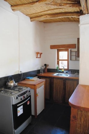 A compact kitchen with a gas stove, a small refrigerator, and a wooden countertop.