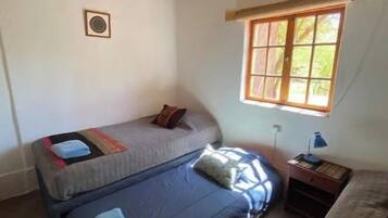 A room with two beds, a window, a lamp, and a small table.