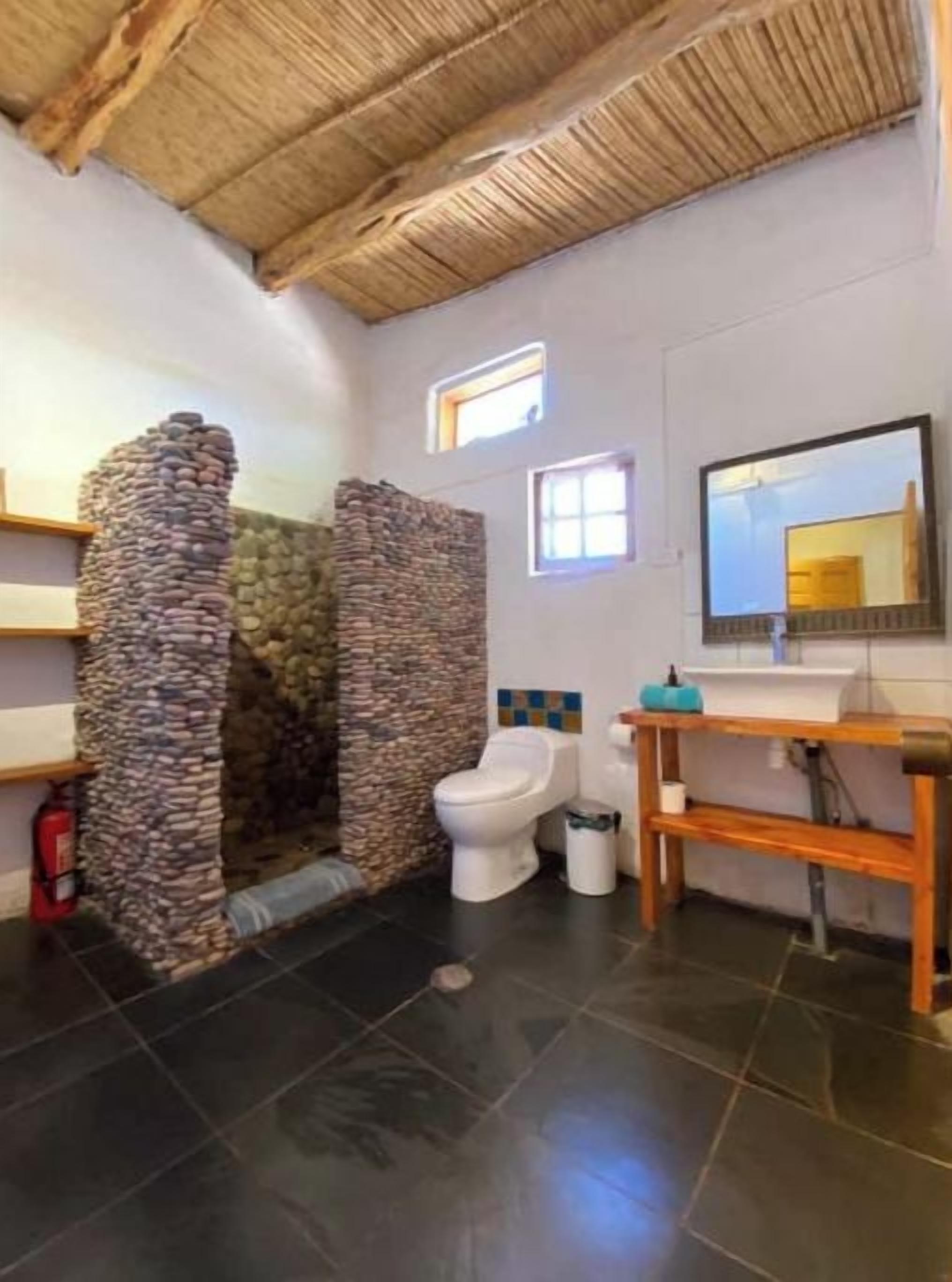 Een badkamer met een stenen muur, toilet, wastafel en spiegel.
