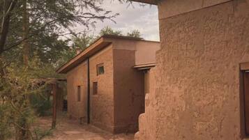 A pathway leading to a rustic building with a stone floor and a natural, unadorned exterior.