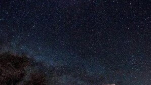 Un edificio con techo plano y varias ventanas, rodeado de una zona de grava bajo un cielo estrellado.