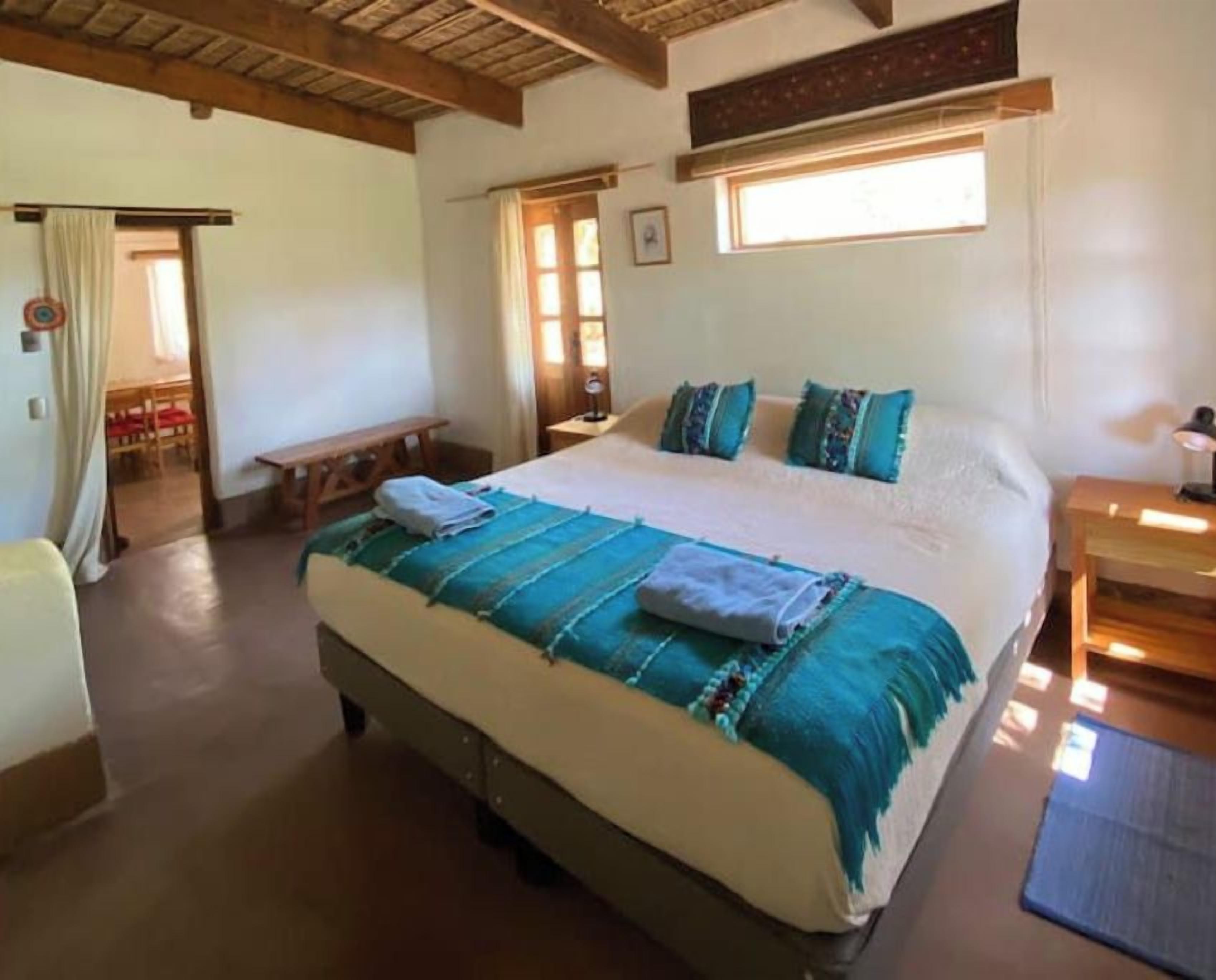 A bedroom with a large bed, a wooden bench, a bedside table, and a window.
