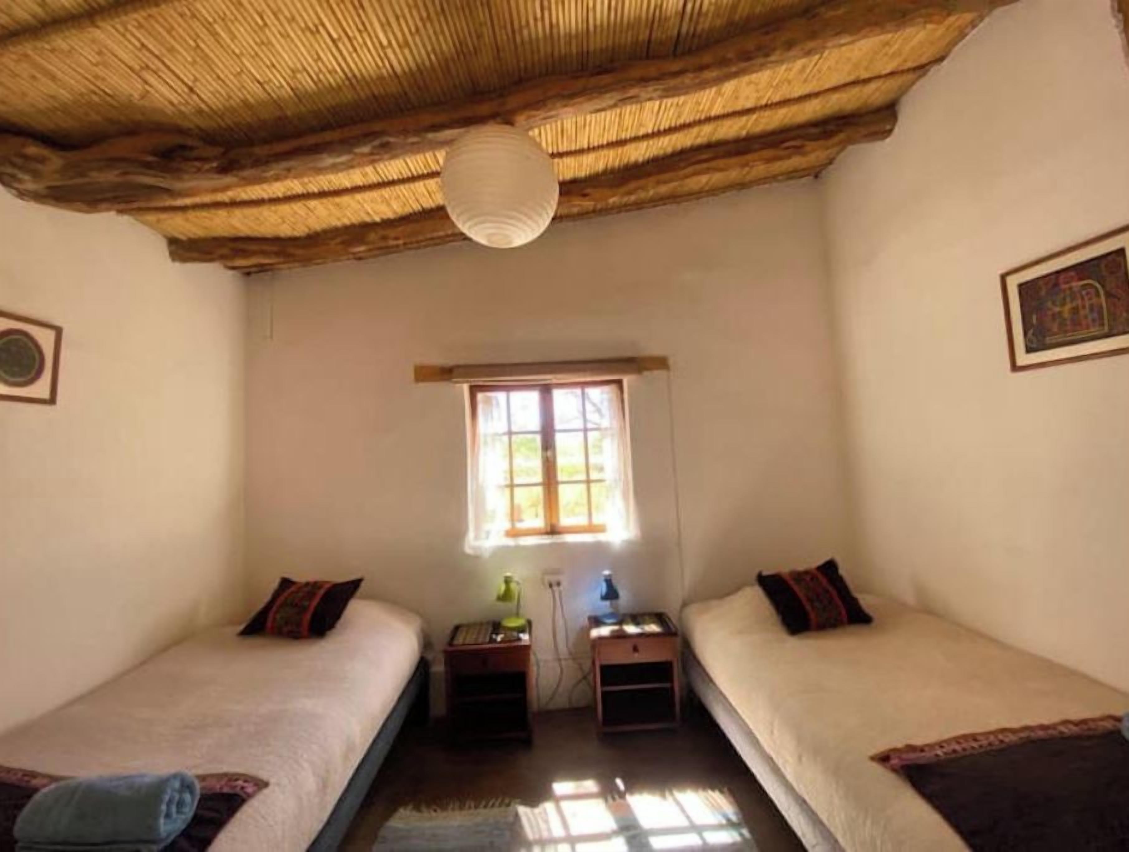 A room with two single beds, a window with natural light, a ceiling fan, and a wall-mounted light fixture.