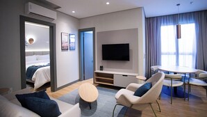 Una habitación de hotel moderna con una cama, un televisor, un rincón de comedor con sillas y una mesita.