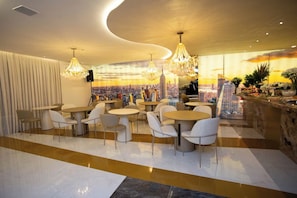 Un restaurant moderne avec des tables et des chaises rondes, une fresque représentant un paysage urbain sur le mur et une vue sur les bâtiments de la ville.