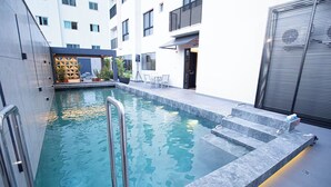 Una piscina interior moderna con agua cristalina, escalones para entrar y una zona de estar con sillas y una mesa.
