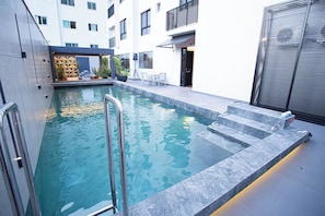 Une piscine intérieure moderne, dotée d’une eau claire, de marches permettant d’y accéder et d’un espace détente avec des chaises et une table.