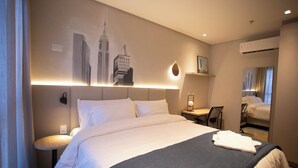 Habitación de hotel con una cama grande, un escritorio y una silla. Hay un cuadro en la pared y un equipo de aire acondicionado.