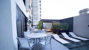 Una terraza en la azotea con piscina, sillones de descanso y una mesa con sillas.