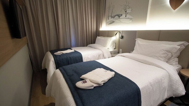 Habitación de hotel con dos camas, un televisor de pantalla plana, una lámpara de pared y un cuadro.