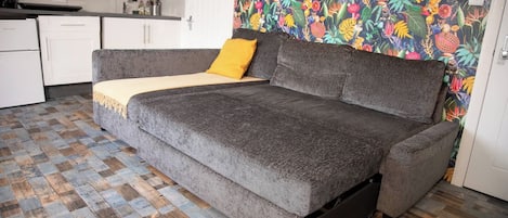 A grey sofa with a yellow throw pillow in a room with a patterned wallpaper and a checkered wooden floor.