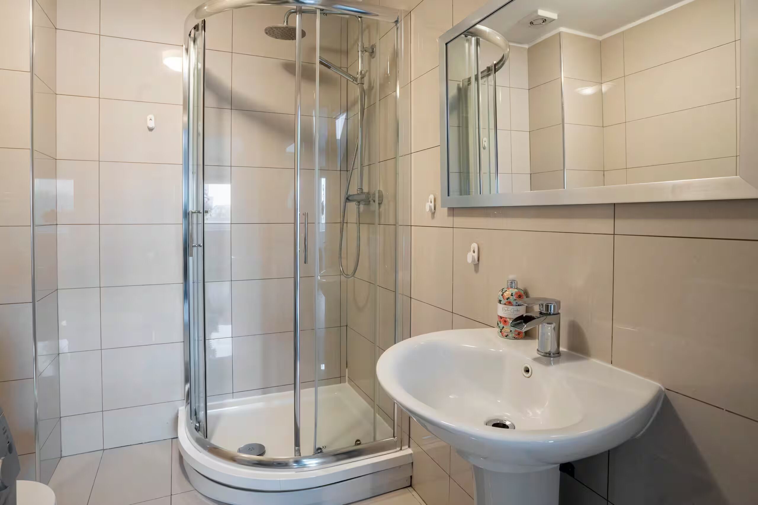 Ein modernes Badezimmer mit einer Duschkabine aus Glas, einem weißen Waschbecken und einem Spiegel darüber.