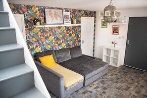 A room with a grey sofa, a yellow throw, a patterned wallpaper, a hanging light fixture, and a staircase. - 3 Bed Flat - 1 Min Walk Underground (London)