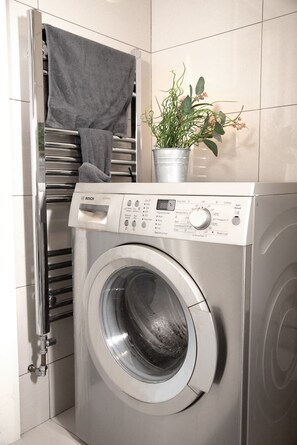 A front-loading washing machine with a control panel, a towel rack, and a potted plant. - 3 Bed Flat - 1 Min Walk Underground (London)