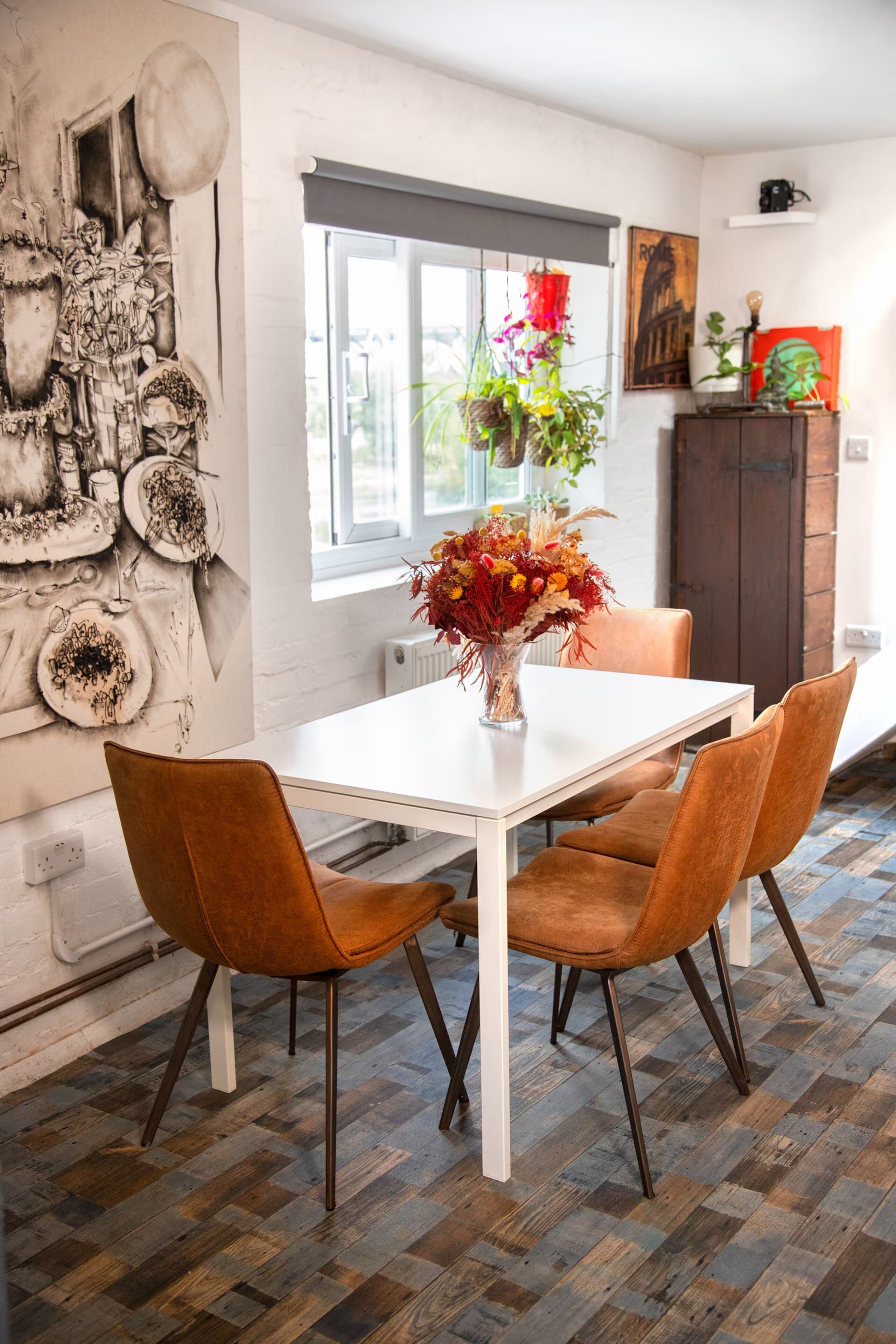 A dining area with a white table and two brown chairs, a vase with flowers, and a wall with various decorations.