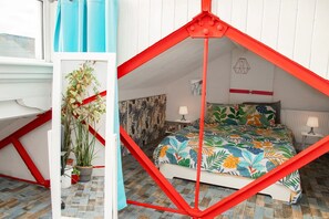 A bedroom with a sloped ceiling, a bed with a floral bedspread, a red metal frame, and a potted plant. - 3 Bed Flat - 1 Min Walk Underground (London)