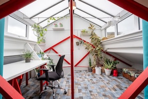 A modern, compact room with a sloped ceiling, a white desk, a black office chair, and various potted plants. - 3 Bed Flat - 1 Min Walk Underground (London)