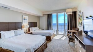Habitación de hotel con dos camas, un escritorio, una silla, un televisor y un balcón con vista al océano.