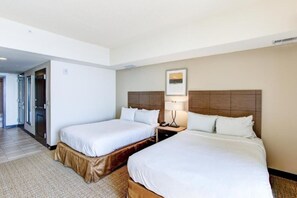 Quarto de hotel com duas camas, uma mesa de cabeceira com abajur e um quadro na parede.
