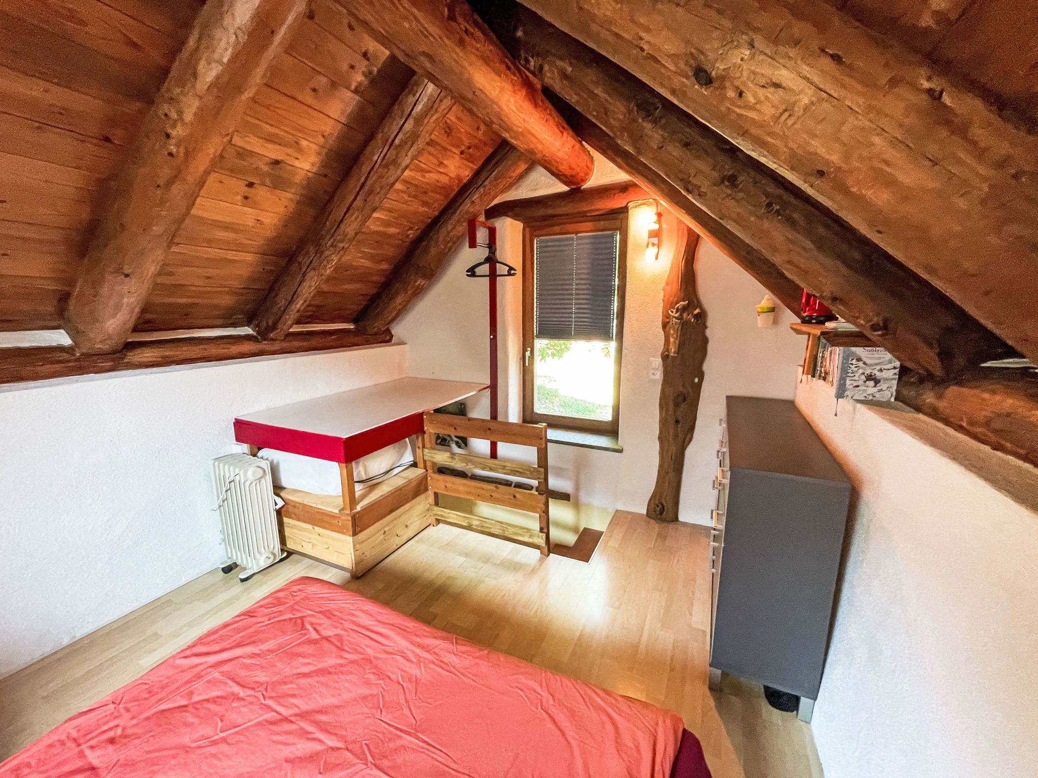Ein kleines, gemütliches Schlafzimmer im Dachgeschoss mit schrägen Wänden, einem Einzelbett, einem Tisch und einer Heizung.