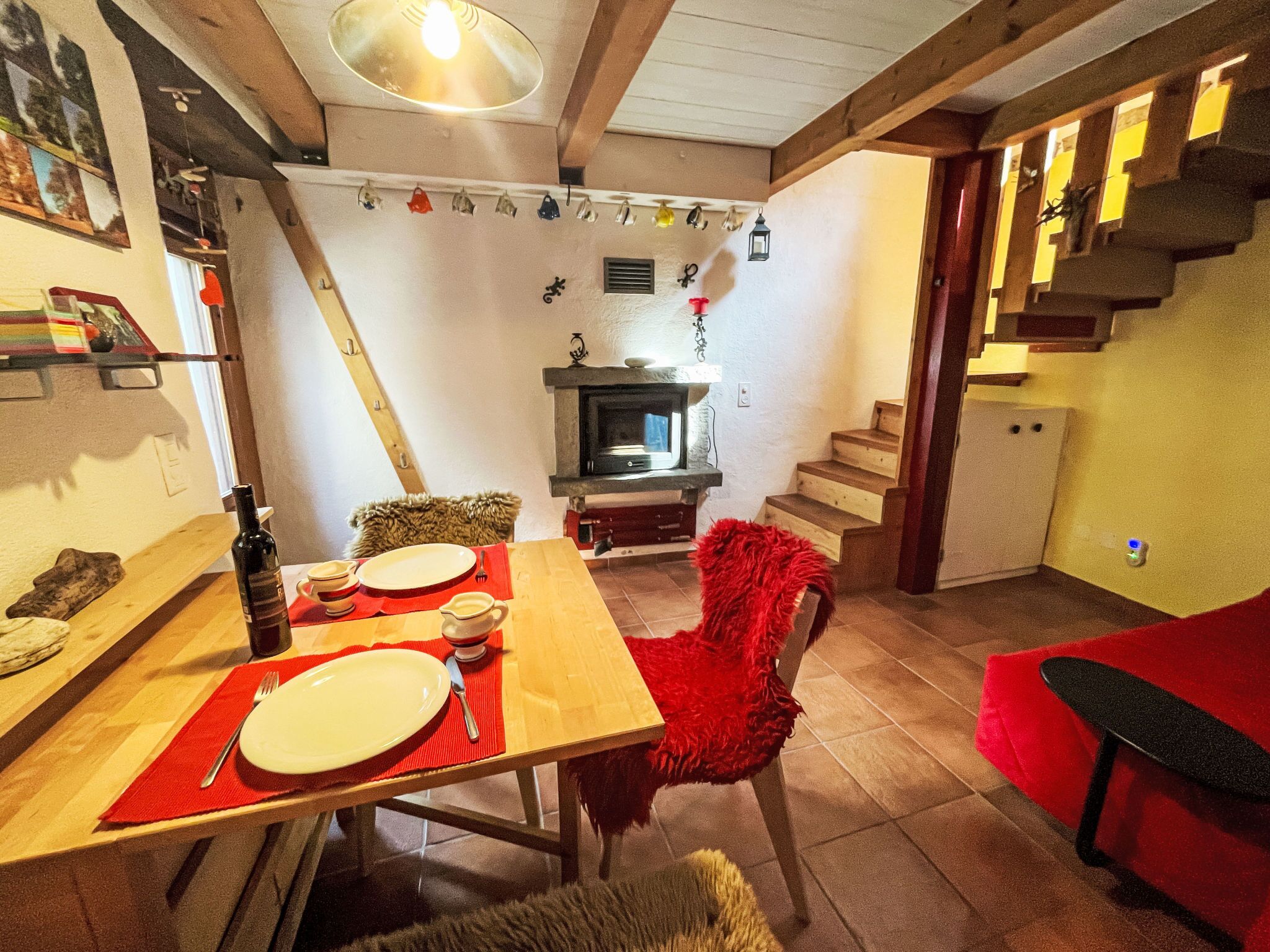 Ein Essbereich mit einem Holztisch für zwei Personen, einem Kamin und einer Treppe, die zu einer oberen Ebene führt.