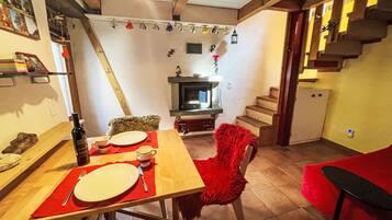 Ein Essbereich mit einem Holztisch für zwei Personen, einem Kamin und einer Treppe, die zu einer oberen Ebene führt.