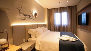 Habitación de hotel con una cama, un escritorio, un televisor de pantalla plana y una obra de arte colgada en la pared.