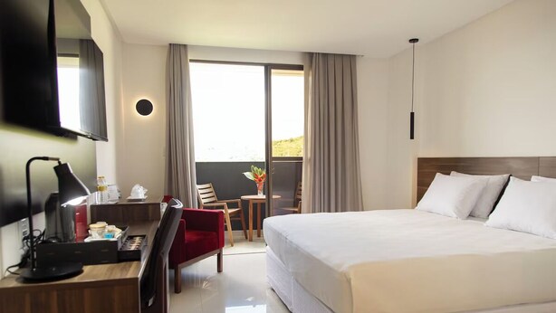 A hotel room with a large bed, a desk with a lamp, a TV, and a balcony with a view. - Stylish Room with Balcony and Buffet Breakfast – Near Main Attractions (Pernambuco)