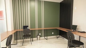 Un espai d'oficina modern amb un escriptori de fusta corbat, dues cadires negres, un ordinador i un safata de recollida de residus.
