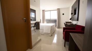 Quarto de hotel com cama, escrivaninha, cadeira e televisão.