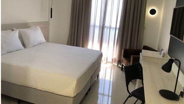 A hotel room with a large bed, a desk with a chair, a desk lamp, and a window with curtains. - Relaxing Room Perfect for Families and Leisure Travelers Visiting Araripina (Pernambuco)