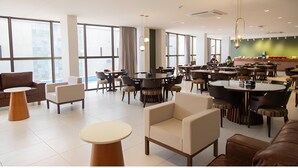 A modern dining area with multiple tables and chairs, large windows, and a green accent wall. - Relaxing Room Perfect for Families and Leisure Travelers Visiting Araripina (Pernambuco)
