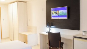 A hotel room with two beds, a desk with a chair, a television mounted on the wall, and a small refrigerator. - Sleek Room Ideal for Exploring Araripina Museum - with 2 Swimming Pools! (Pernambuco)