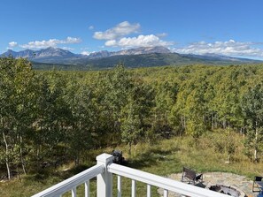 A deck with a stone fire pit and chairs, overlooking a forested area with mountains in the distance. - Glacier Aurora - Stargazing Wonder overlooking the Forest and the East Rockies (Babb)