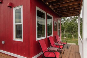 Un bâtiment rouge avec des ornements blancs, un porche couvert et des chaises rouges.
