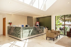 A modern reception area with a marble counter, seating, and a view of greenery through large windows.