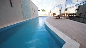A swimming pool with a tiled edge, surrounded by a patio with wooden chairs and tables. - Unwind in a Bright Space with Balcony & Buffet Breakfast Near Local Attractions (Pernambuco)