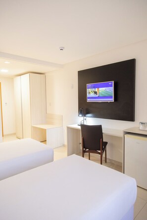 Ett hotellrum med två sängar, ett skrivbord med en stol, en tv som är monterad på väggen och ett litet kylskåp.