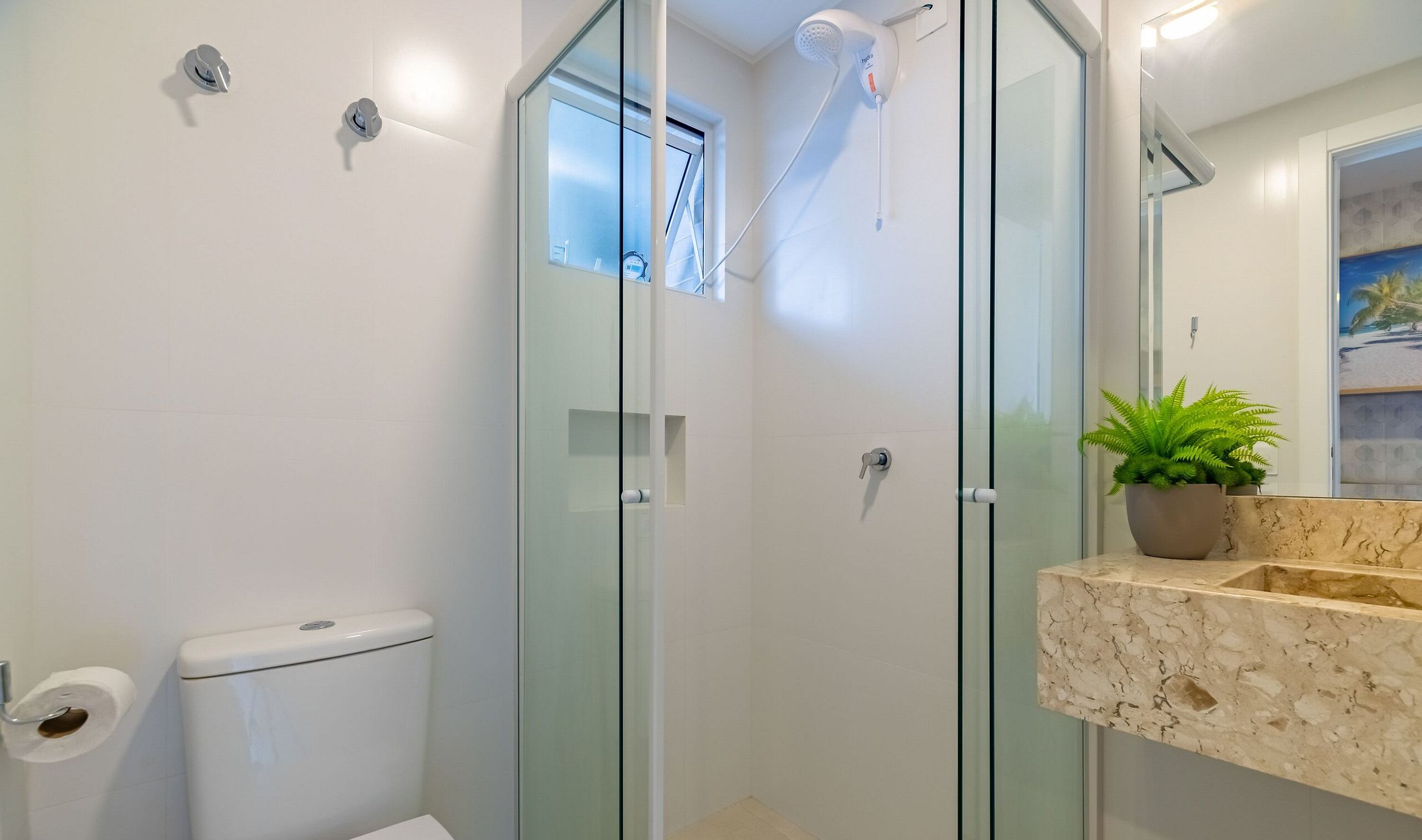 Un baño moderno con ducha de vidrio, inodoro y lavamanos de mármol con planta en maceta.
