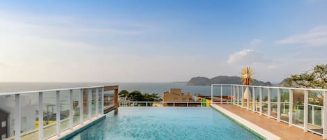 A rooftop infinity pool with a clear view of the sea and distant land.