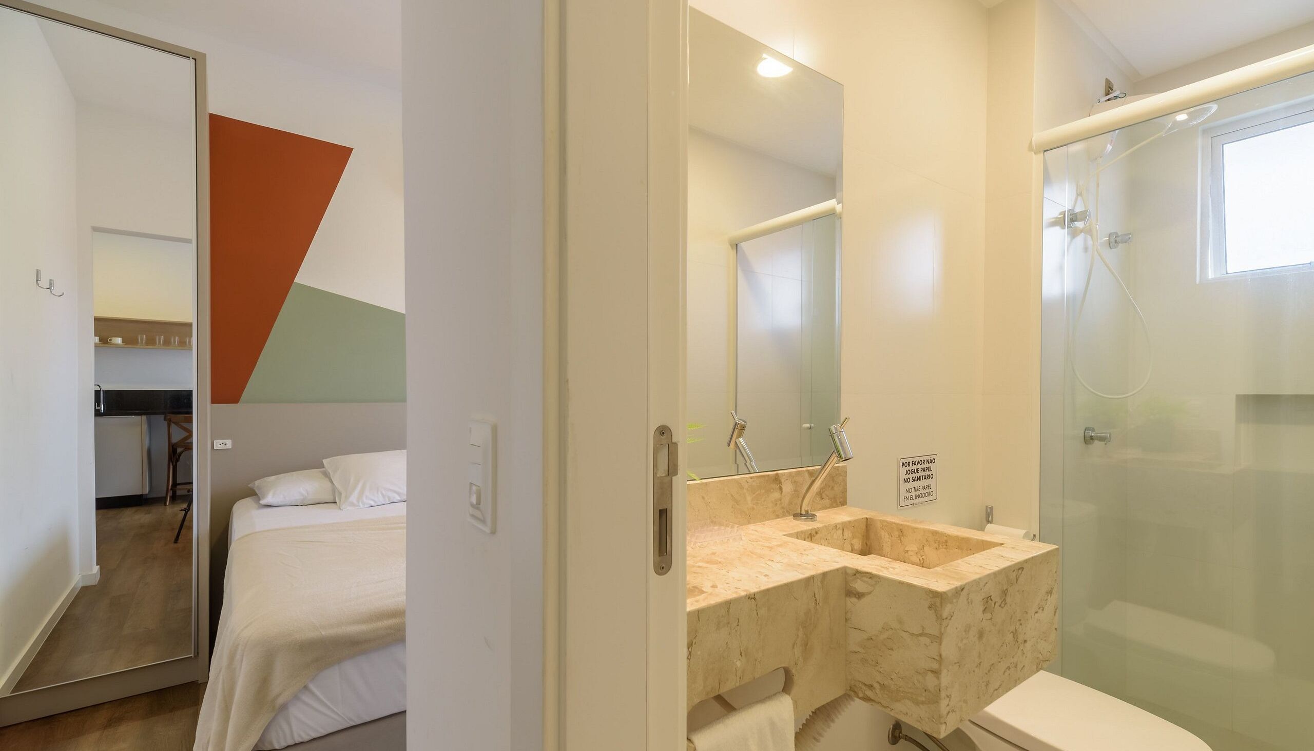 A hotel room with a bed, a bathroom with a glass shower enclosure, and a mirror.