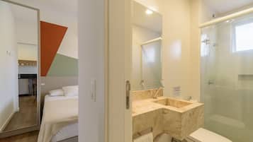 A hotel room with a bed, a bathroom with a glass shower enclosure, and a mirror.