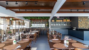 A restaurant interior with wooden tables and chairs, a bar area with shelves of bottles, and a green hanging plant. - Studio w/ Pool nr Beach Bombinhas Vec112 (Bombinhas)