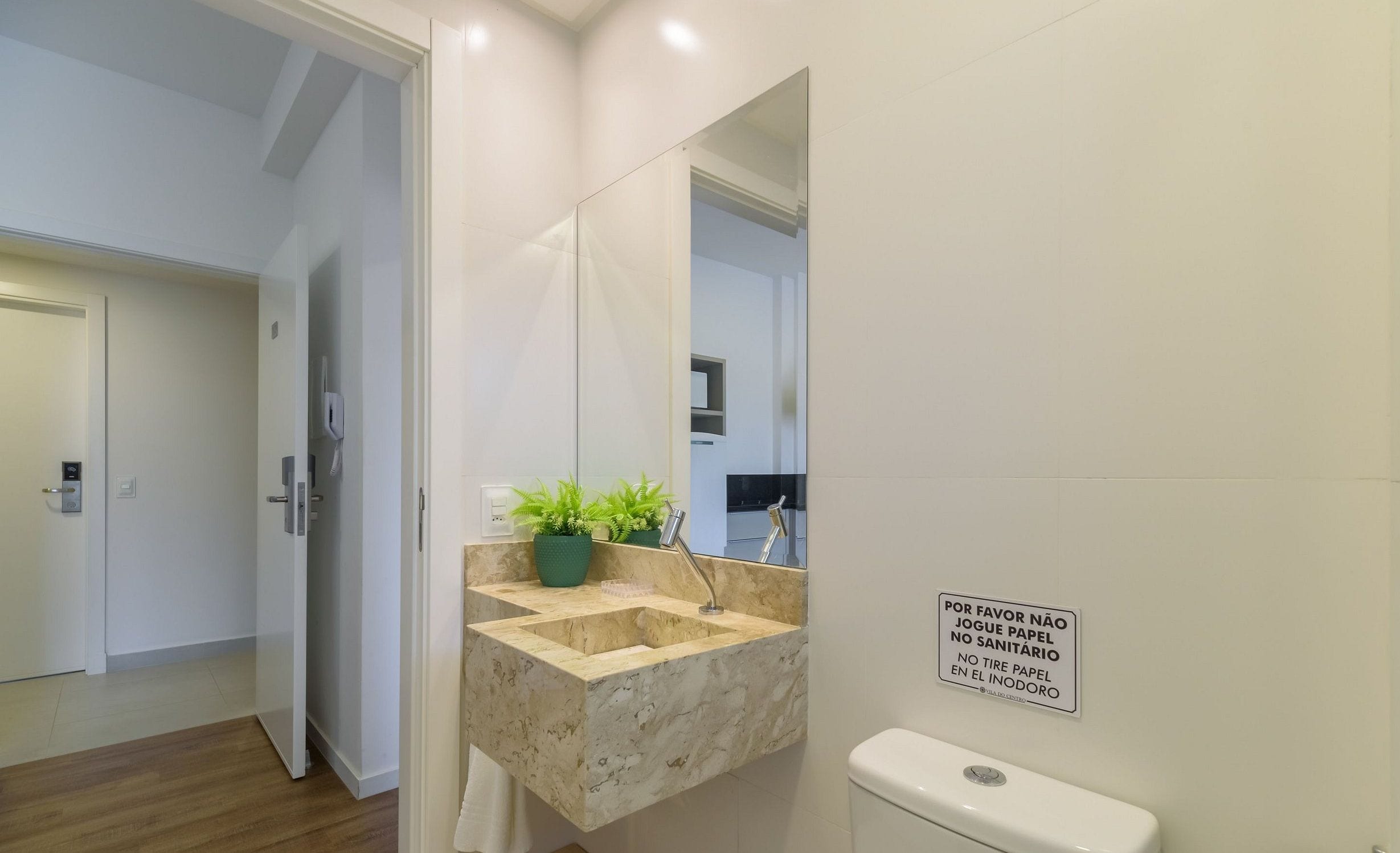 A modern bathroom with a marble sink, a green plant, and a toilet. There's a sign on the wall with text in a foreign language.