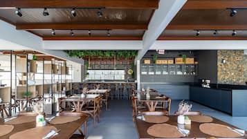 A restaurant interior with wooden tables, chairs, a bar area, and a hanging plant.
