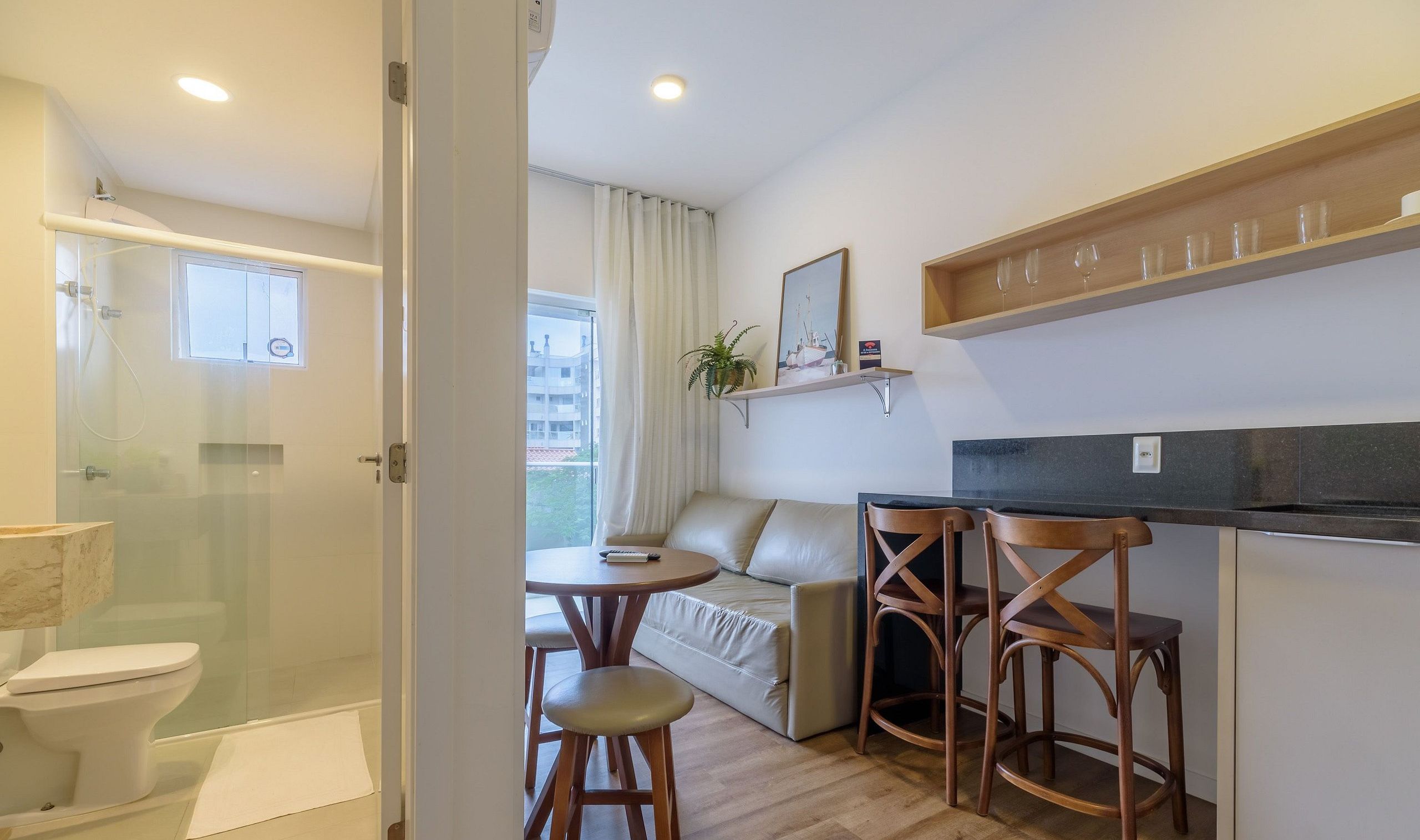 A compact hotel room with a shower, toilet, and a small dining area with a sofa and two wooden chairs.