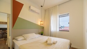 A hotel room with a bed, a window with curtains, an air conditioning unit, and a plant on the nightstand. - Studio w/ Pool nr Beach Bombinhas Vec112 (Bombinhas)
