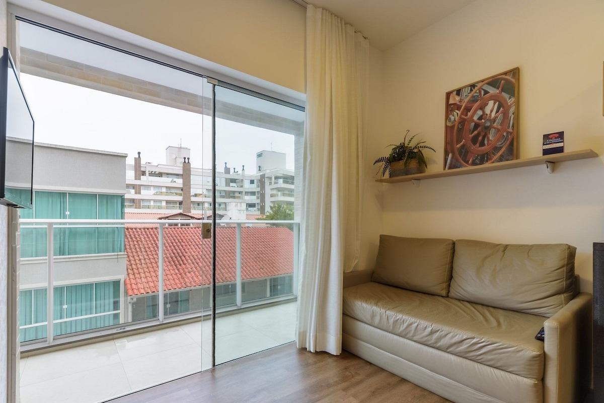 A living room with a sliding glass door leading to a balcony, a beige sofa, a mounted television, and a framed picture on the wall.