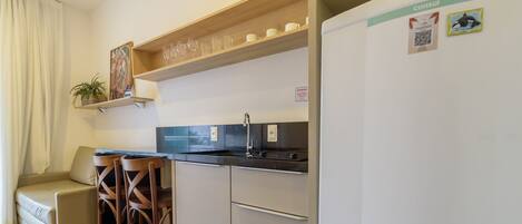 Una cocina compacta con un lavamanos, un refrigerador y un estante de madera sobre la encimera.