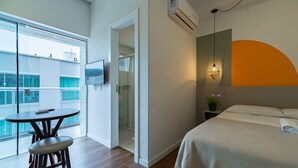 Hotellihuone, jossa on sänky, pieni pöytä ja tuoli, seinälle asennettu televisio ja ilmastointilaite.